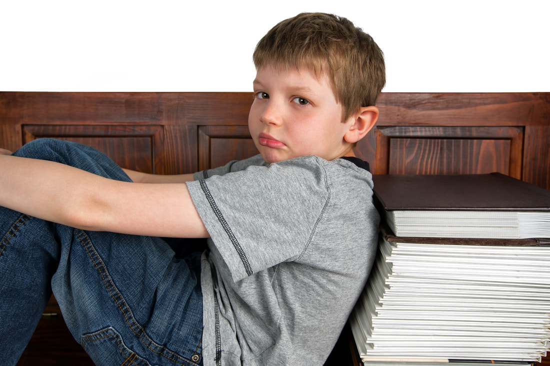 Picture of child looking sad next to a pile of books.